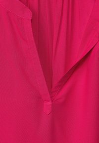 Blusa fucsia con escote en V y diseño plisado. Tejido suave con un brillo sutil y detalles de costura en contraste.