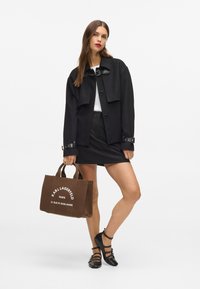 Melna vilnas sajaukuma īsā jaka ar pogu aizdari, saskaņota ar pieguļošu melnu svārku. Brūnas auduma somiņas ar baltu tekstu un logo. Melnas dzīvokļu kurpes.