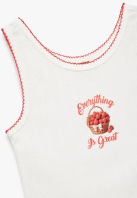 Vit ärmlös topp med röd scalloped trim och grafiskt motiv av en korg med jordgubbar med texten "Allt är bra" på framsidan.
