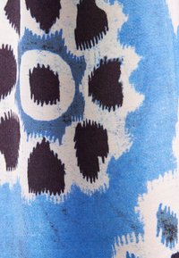 Tissu bleu avec des motifs floraux abstraits en dents de scie en blanc et noir, présentant des formes irrégulières et des bords texturés.