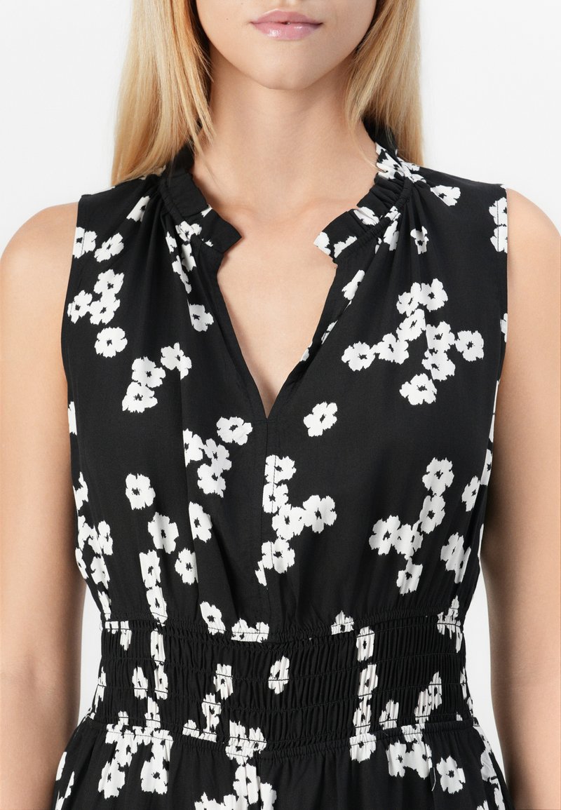 Schwarzes ärmelloses Kleid mit floralem Muster in Weiß, mit einem V-Ausschnitt und gerafftem Taillenteil für eine lockere Passform. Glatte Stofftextur.