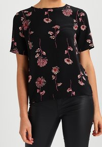 Black short-sleeve blouse with pink floral pattern paired with black fitted pants, shown from neck to hips.
