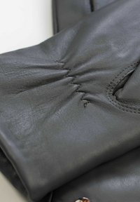 Gray leather gloves feature stitched detailing at the wrist, with smooth texture and rounded fingertips, showcasing a minimalist design.