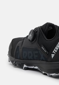 Black athletic shoe made of synthetic mesh and rubber, featuring a BOA dial closure, textured material, and a rugged outsole with traction.