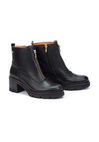Botas de tobillo de cuero negro con dos cremalleras doradas, un tacón de bloque texturizado y una superficie suave con un forro interior marrón.