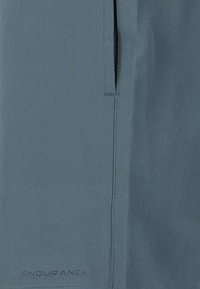 Ljusbl�å utomhusbyxor i en slät, teknisk tyg, med en ficka med dragkedja och "ENDURANCE"-logotyp nära fållen.