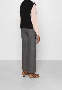 Gilet sans manches noir en tricot, blouse à manches longues rose pâle, pantalon large en pied-de-coq gris et sandales à talons strappés marron clair avec des accents argentés.