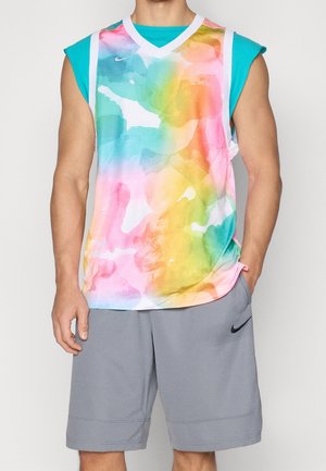 Ärmelloses Basketballtrikot in mehrfarbigem Batikmuster über einem türkisfarbenen ärmellosen Shirt, kombiniert mit grauen Nike-Shorts, Modell steht mit einer Hand in der Tasche.