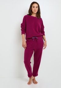 Sweatshirt violet avec une coupe décontractée et une texture côtelée, associé à un pantalon assorti avec une taille à cordon de serrage et des poignets roulés.