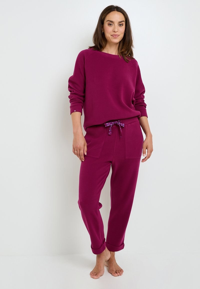 Sweatshirt violet avec une coupe décontractée et une texture côtelée, associé à un pantalon assorti avec une taille à cordon de serrage et des poignets roulés.