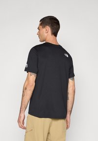 Tricou negru cu mânecă scurtă și guler rotund, având un mic logo alb pe partea superioară a spatelui și pe braț. Textură de material neted.