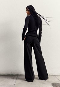 Čierny rebrovaný top s dlhým rukávom, skombinovaný s voľnými čiernymi džínami. Oblečenie má priliehavý strih a gombíkové detaily na rukávoch.