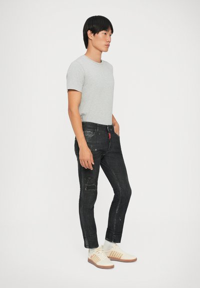 Camiseta gris de manga corta, vaqueros negros desgastados, zapatillas blancas con detalles en marrón. Ajuste casual, textura suave, diseño ajustado.