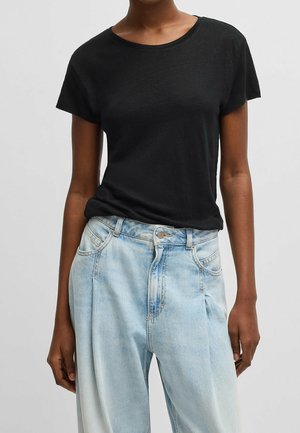 Persona que lleva una camiseta negra ajustada de manga corta metida en unos vaqueros de mezclilla descoloridos de color azul claro de tiro alto con bolsillos delanteros.
