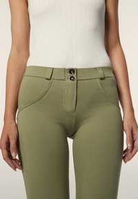 Vihreät puuvillasekoitehousut, joissa on kaksi mustaa nappia vyötäröllä. Housuissa on viistot etutaskut ja sileä, teksturoitu pinta.