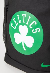 Zaino nero con un logo circolare verde prominente e un trifoglio bianco, con la scritta "CELTICS" sopra, realizzato in materiale durevole.