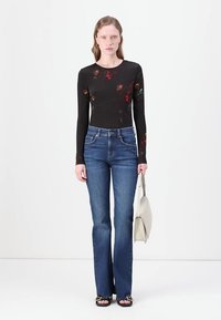 Top negro de manga larga con estampado floral, combinado con jeans acampanados azules. La modelo sostiene un bolso de color claro y lleva sandalias de tacón abierto.