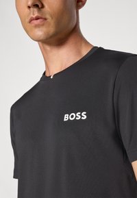 Svart kortermet t-skjorte laget av glatt stoff, med en hvit "BOSS" logo på venstre bryst og rund halslinning med en liten detalj.