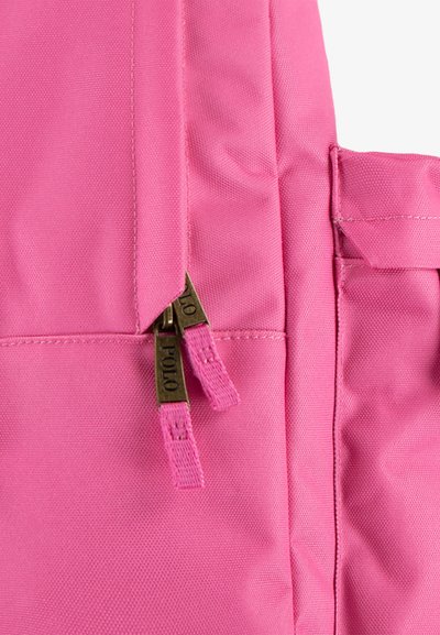 Ροζ σακίδιο φτιαγμένο από ύφασμα, με φερμουάρ και μπρονζέ μεταλλικά στοιχεία, εξωτερικές τσέπες και υφή για αυξημένη αντοχή.