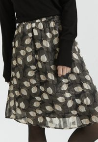 Jupe noire à taille froncée, avec un motif de feuilles beiges et de fines lignes, réalisée en tissu léger et translucide.