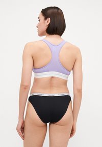 Fialový športový top s bielym pásom, dizajn s prekríženými ramienkami; skombinovaný s čiernymi nohavičkami s bielym pásom s logom Calvin Klein. Hladká textúra.