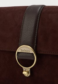 Brązowa torba z zamszu z ciemnobrązowym skórzanym paskiem i zatrzaskiem z mosiądzu. "Barbour" wyryte na metalowych elementach.