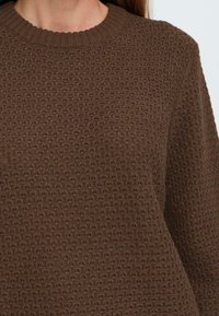 Brauner Strickpullover mit strukturiertem Oberflächen- und Rippkragen. Der Stoff weist ein erhabenes Muster für zusätzliche Dimension auf.