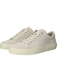 Suede sneakers in light beige with rounded toe, white laces, and a textured rubber sole. Features minimal branding on the heel.