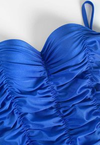 Niebieski kostium kąpielowy z marszczeniami, charakteryzujący się gładką, błyszczącą teksturą. Wycięcie w kształcie serca z cienkimi, regulowanymi ramiączkami.