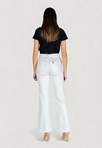 Biele rozšírené rifle s vysokým pásom, zadnými vreckami a jemnou rebrovanou textúrou; kombinované s priliehavým čiernym tričkom. Jasná silueta zozadu.