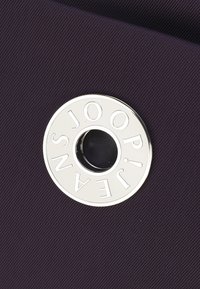 Logo in metallo argentato con ritaglio, testo in rilievo, su uno sfondo di tessuto textured di colore viola scuro, caratterizzato da una forma circolare.