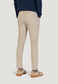 Pantalones beige de corte ajustado, con bolsillos traseros y textura suave. Combinados con zapatos beige claros y calcetines grises.