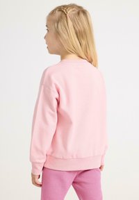 Roze sweatshirt met lange mouwen, ribgebreide boorden en een ronde halslijn. Zacht, textuurstof. Draagt met roze nauwsluitende leggings.