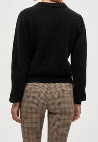 Svart, fluffig stickad tröja med avslappnad passform och rund halsringning, i kombination med bruna rutiga byxor med en strukturerad yta.