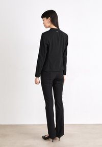 Black tailored jacket with a straight cut, featuring long sleeves and a subtle back seam detail, paired with flared black pants and closed-toe heels.