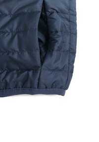 Tissu de veste matelassée bleu marine avec une texture lisse et des détails de couture visibles, montrant un poignet et une partie de l'ouverture de la manche.