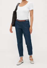 Džínové kalhoty v tmavě modré barvě s volným střihem, ohrnuté manžety, hnědý pásek se zlatým kováním, bílá tričko a světle béžové boty.