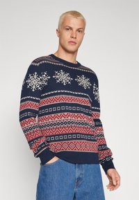 Maglione lavorato a maglia di colore blu scuro con motivi a fiocco di neve bianchi e rossi e motivi geometrici, maniche lunghe, polsini a costine e colletto rotondo.