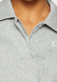 Grå polo t-shirt i mjukt tyg med en vikbar krage, två knappar och en liten broderad logotyp på vänster bröst.