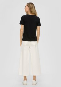 Schwarzes T-Shirt mit kurzen Ärmeln, kombiniert mit weiten, cremefarbenen Hosen. Das Outfit hat ein einfaches Design mit minimalen Details. Weiße Sneakers runden den Look ab.