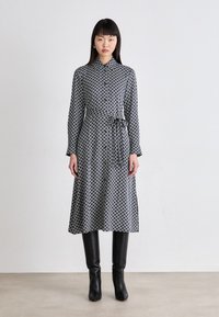 Vestito a maniche lunghe con colletto in blu navy con motivi geometrici, cintato in vita con una cintura. Abbinato a stivali neri alti fino al ginocchio.