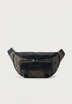 Sac banane en tissu à motif marron foncé, avec dessus en cuir noir et poche à rabat avant, double fermeture éclair et deux attaches à boucle noires.