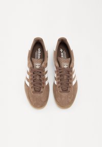 Sneakers in camoscio marrone con tre strisce bianche, punta rotonda e suola in gomma color naturale. Presentano colletto imbottito e etichetta con marchio sulla linguetta.