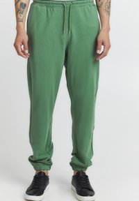 Grønne sweatpants laget av myk stoff, med elastisk midje, justerbar snor og smale mansjetter. Kombinert med svarte joggesko.