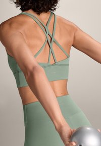 Mintgroene sporttop met gekruiste banden op de rug, met een soepele textuur en subtiele branding op de band.