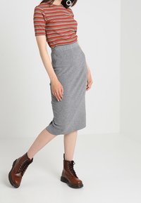 Pruhovaný červený a šedý top s krátkým rukávem v kombinaci se šedou tužkovou sukní, doplněný hnědými šněrovacími kotníkovými botami. Jednoduchý, přiléhavý design.