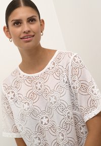 Weiße Spitzenbluse mit floralen Mustern, kurzen Ärmeln, rundem Ausschnitt und aufwendigen Durchbrüchen für einen zarten Look.