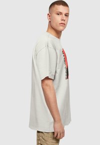 Lichtgrijs katoenen t-shirt met korte mouwen, een relaxed fit, met een grafisch ontwerp in rood en zwart op de voorkant.