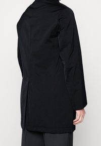 Schwarze, langärmlige Jacke mit einer glatten, matten Textur, die ein tailliertes Design und geraden Schnitt aufweist. Der Rücken hat einen dezenten Schlitz.