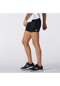 Pantalones cortos deportivos negros con acentos de malla, que presentan un pequeño logo blanco, combinados con zapatillas de correr negras con detalles grises y suelas blancas.